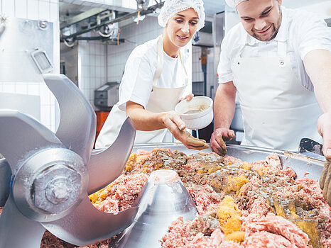 Zwei Arbeiter, die Fleisch in einer Maschine verarbeiten